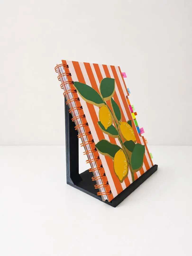 Black 3D printed notebook display stand holding a colourful spiral notebook